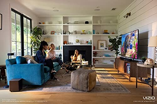 Three people in a modern living room watching TV and playing video games.